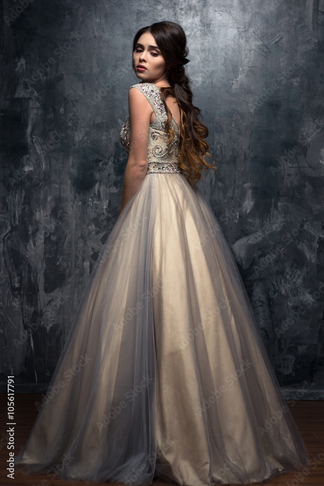 Fashion beauty portrait of gorgeous young woman with long curly hair in luxury evening dress