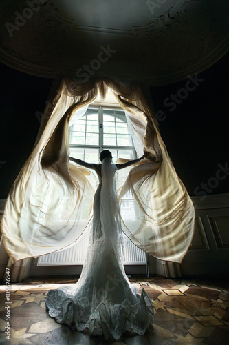 Gorgeous happy bride in white dress opening curtains in theatre