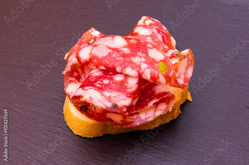 Slice of bread with slices of salami with pistachios on top in slate