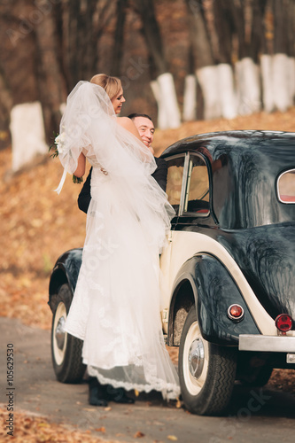 Stylish wedding couple, bride, groom kissing and hugging near retro car in autumn © olegparylyak