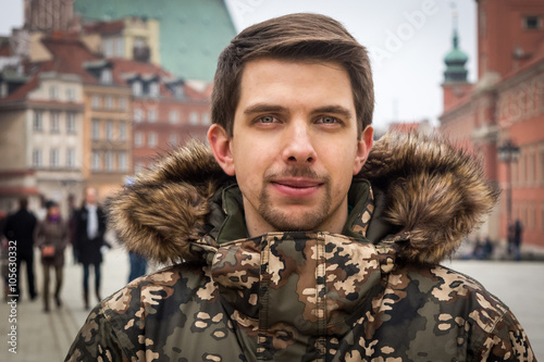 The young man from Warsaw (Poland) in a winter jacket in the old town, the royal castle in the background