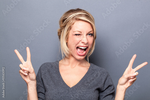 wink and self-confidence concepts - flirting young woman winking and making the v-sign for cool attitude, gray background studio