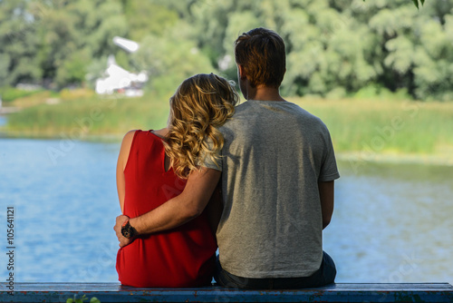 Young and happy couple sitting on the bench hugging. River background