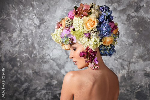 young woman with magnificent flowers bouquet on her head. Woman with bared shoulders, standing back