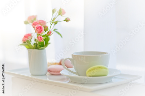 white cup, roses and macaroons near a window