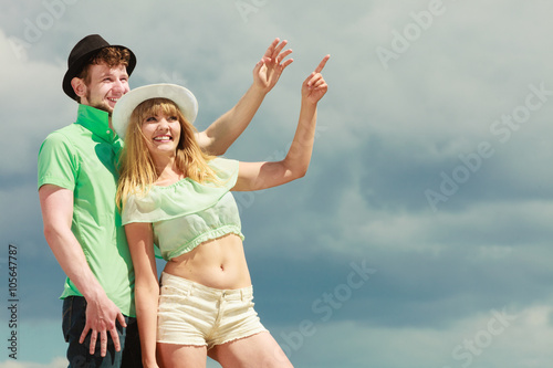 Young couple looking up showing with finger outdoor