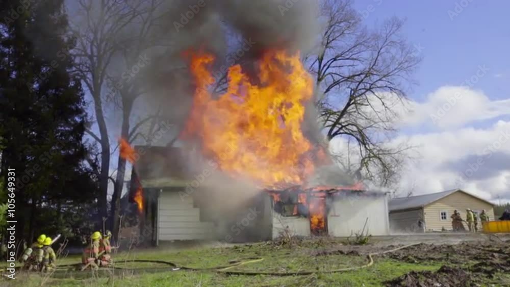 Firemen spray water on a burning house from the front and back 