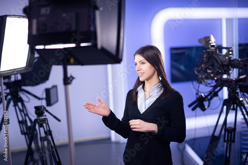 Television presenter recording in television news studio.Female journalist anchor presenting business report.News camera,light equipment behind the scenes.Talking at camera to the TV audience