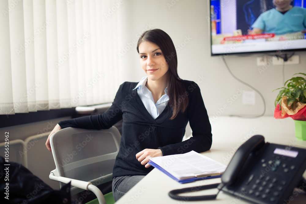 Young smiling female worker in the office.Modern entrepreneur business woman sitting in the office.Customer service representative.Bright office room.Secretary,agent,assistant,phone answering concept