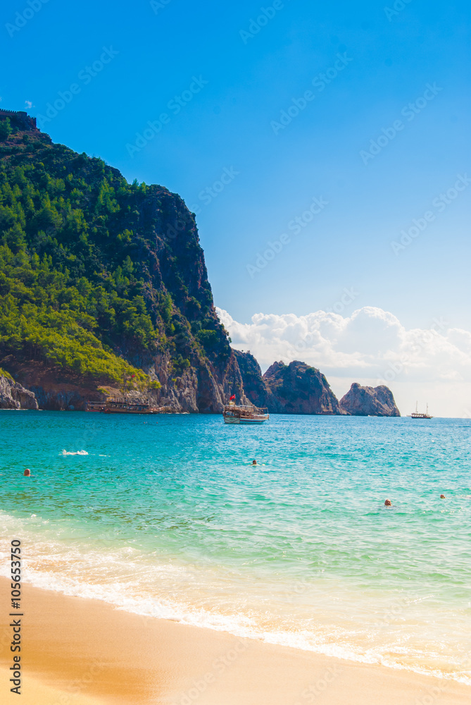 Beach of Cleopatra with sea and rocks of Alanya peninsula, Antalya, Turkey. Beautiful landscape of tourist destination with high green cliff and Castle of Alanya.