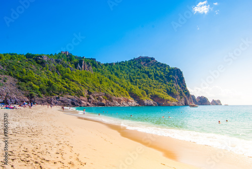 Beach of Cleopatra with sea and rocks of Alanya peninsula  Antalya  Turkey. Beautiful landscape of tourist destination with high green cliff and Castle of Alanya.