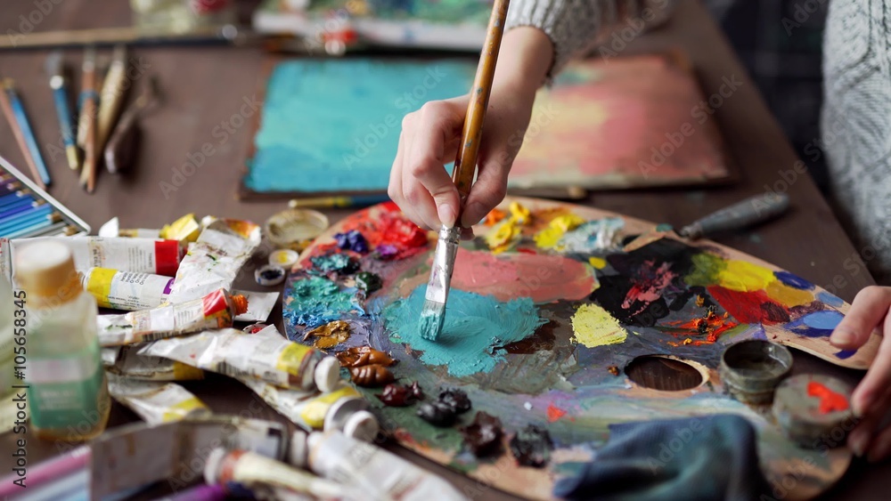 Closeup of paintbrush in woman hands mixing paints on palette