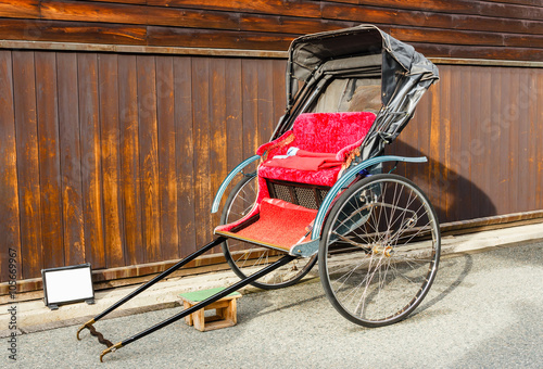 Japanese rickshaw parked beside wall.