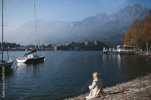 girl sitting on the shore of a mountain lake Como with yachts
