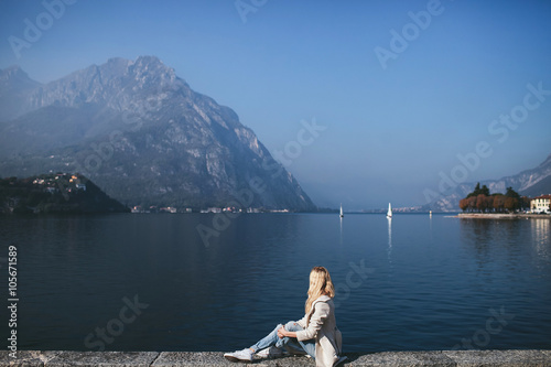 blond woman in coat sitting against the background of a mountain lake Como