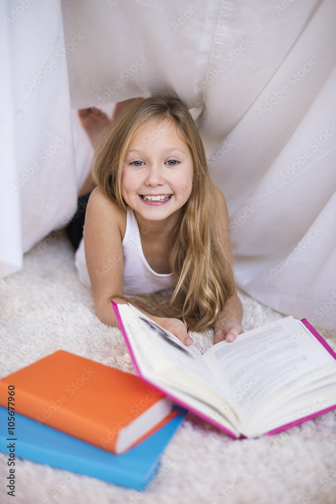 Cheerful girl reading book in a handmade shelter Cheerful girl reading book in a handmade shelter