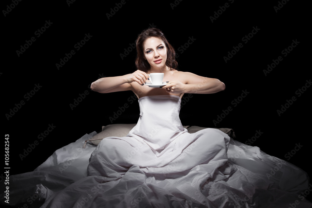 Naklejka premium young female sitting in bed and drinking coffee;