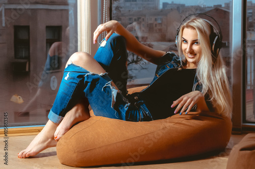 Fun blond woman with beautiful smile posing on couch and listeni photo