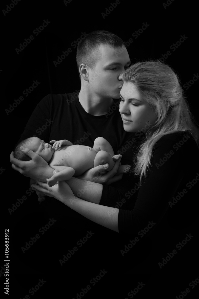 happy family , young parents holding a newborn baby in her arms and gently hugged him, black and white photo on a black background . happy family , young parents holding a newborn baby in her arms and gently hugged him, black and white photo on a black background .