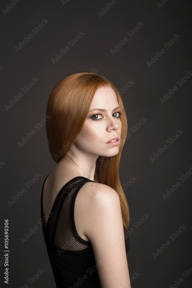 Portrait of attractive red haired woman looking at camera over shoulder. Black background Portrait of attractive red haired woman looking at camera over shoulder. Black background
