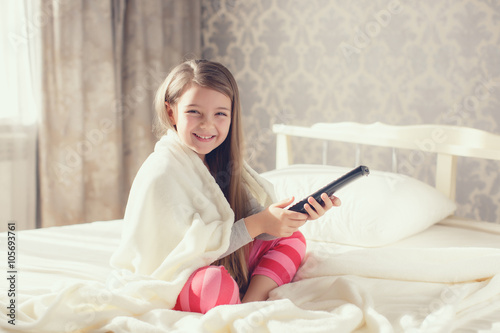 Little girl lying in bed with a remote control TV