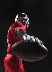 American football player posing with ball on black background