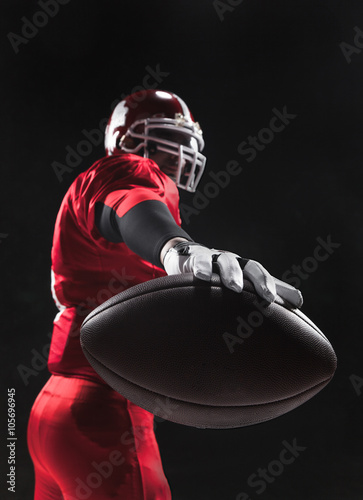 Obraz na płótnie American football player posing with ball on black background