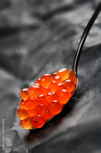Red caviar in a metal spoon on a grey background vertical