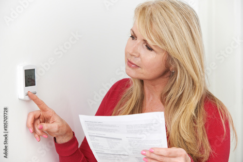 Worried Woman With Heating Bill Turning Down Thermostat