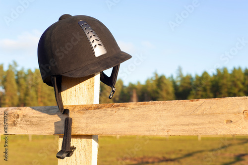 Equestrian helmet forgotten hanging on the wooden fence. photo