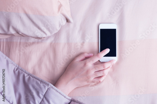 Woman hand under blanket being woken by mobile phone in bedroom.