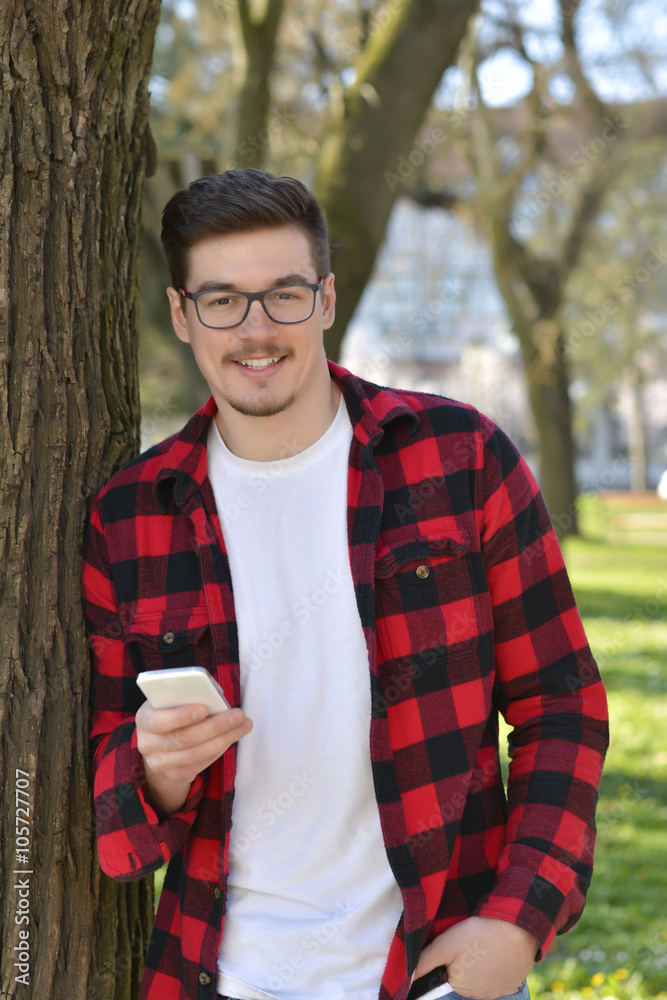 Outdoor portrait of modern young man with mobile phone in park