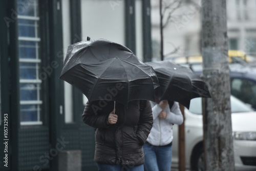 People walking on the street with their open umbrellas on a stormy day 