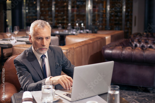 Cheerful old bearded man is working with a notebook