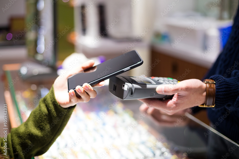 Obraz premium Woman paying with NFC technology on smart phone at shop