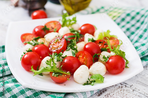 Caprese salad tomato and mozzarella with basil and herbs on a white plate