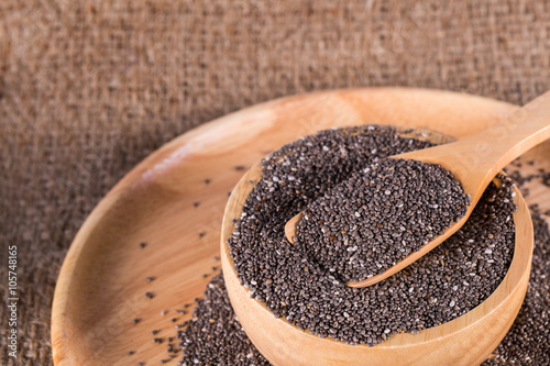 chia seed in wooden bowl on wooden plate and wooden spoon of chia seeds on top. selective focus. on burlap background.