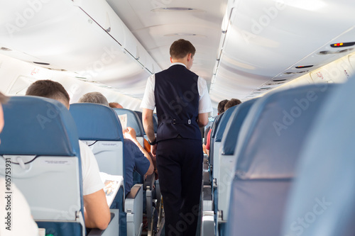 Interior of airplane with passengers on seats and steward walking the aisle.  photo