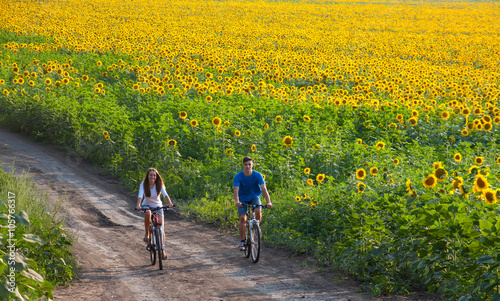 Teen couple riding bike in sunflower field