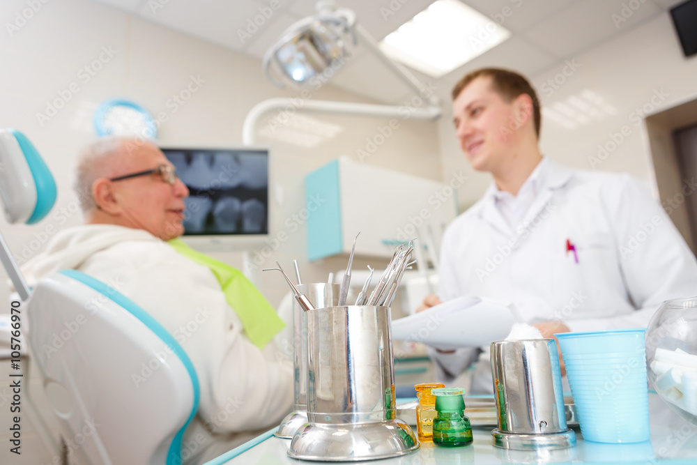 Elderly man on a review of a dentist, sitting in a chair. Focus on a dental tools Elderly man on a review of a dentist, sitting in a chair. Focus on a dental tools