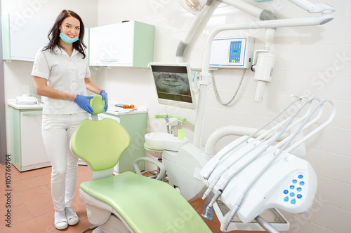 Portrait of a smiling young dentist woman leaning against dentist s chair in dental clinic