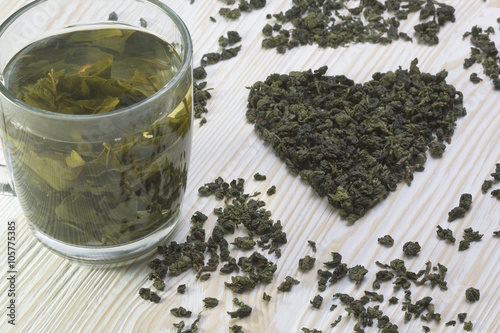 Green tea leaf in shape heart , mug on wooden background