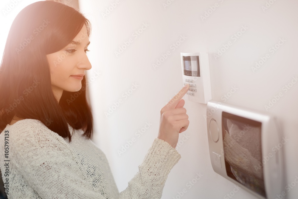 woman entering code on keypad of home security alarm - obrazy, fototapety, plakaty 