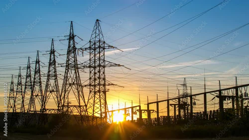 Time-lapse of sunset on a power plant. Sun going through electric high voltage pylon power transmission towers lines. Urban landscape. Electricity production and transportation, transmission. Part 1.