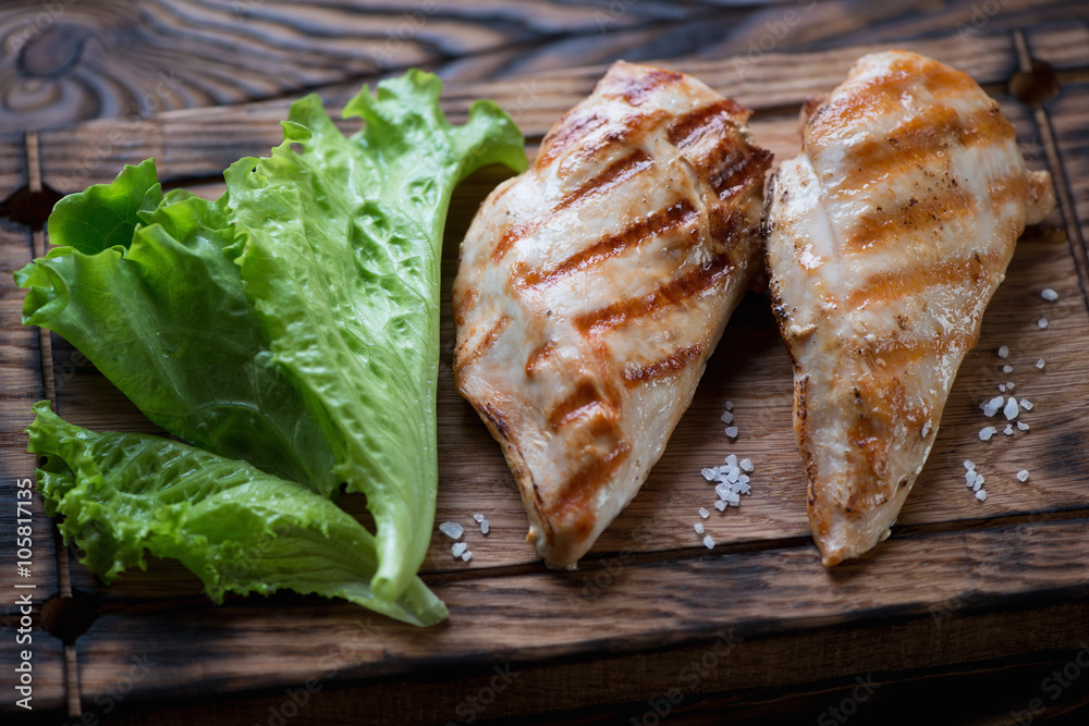 Closeup of grilled chicken breasts served with fresh green salad