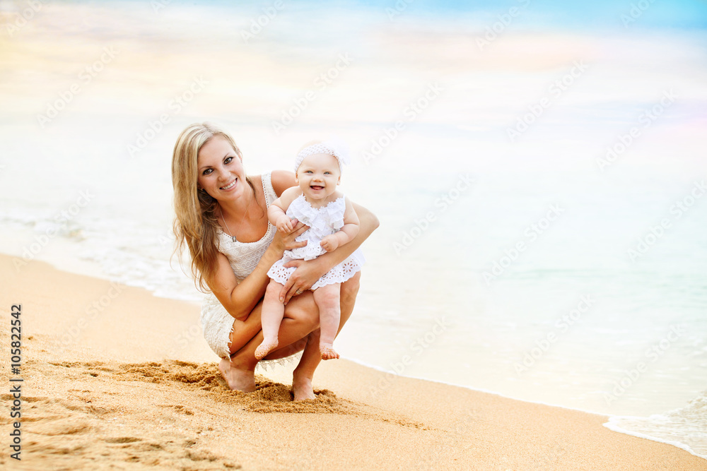 Happy mother and baby girl sitting on beach near sea Happy mother and baby girl sitting on beach near sea
