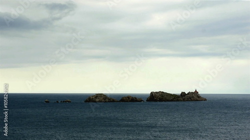 View at lighthouse on small rocky island with dark clouds above
