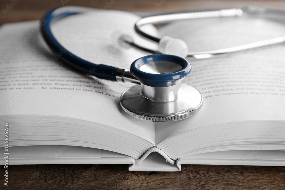 Stethoscope with open book on wooden background. Medical literature concept Stethoscope with open book on wooden background. Medical literature concept