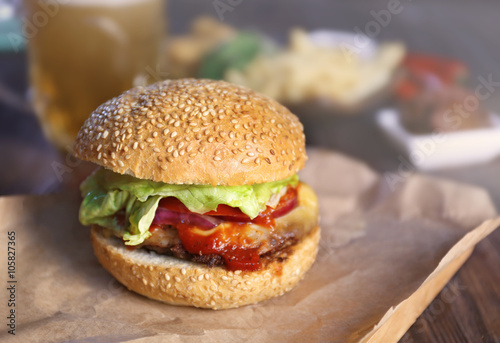 Big tasty hamburger on a paper with light beer in glass mug, close up