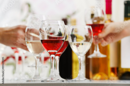 Glasses with different kind of wine and human hands holding wineglasses in the background